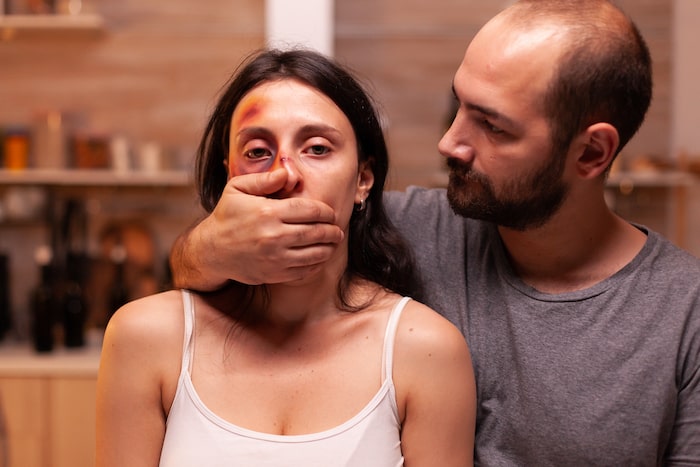 man covering up beaten up woman's mouth